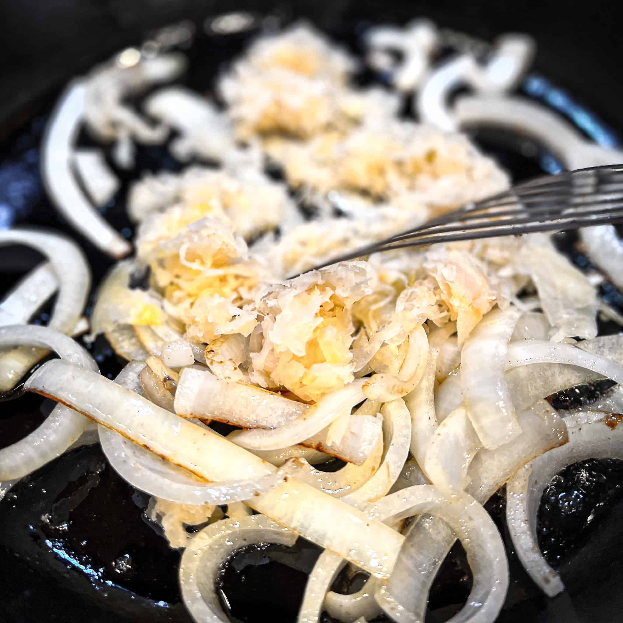 Adding sauerkraut to sauteed onions in cast iron pan.