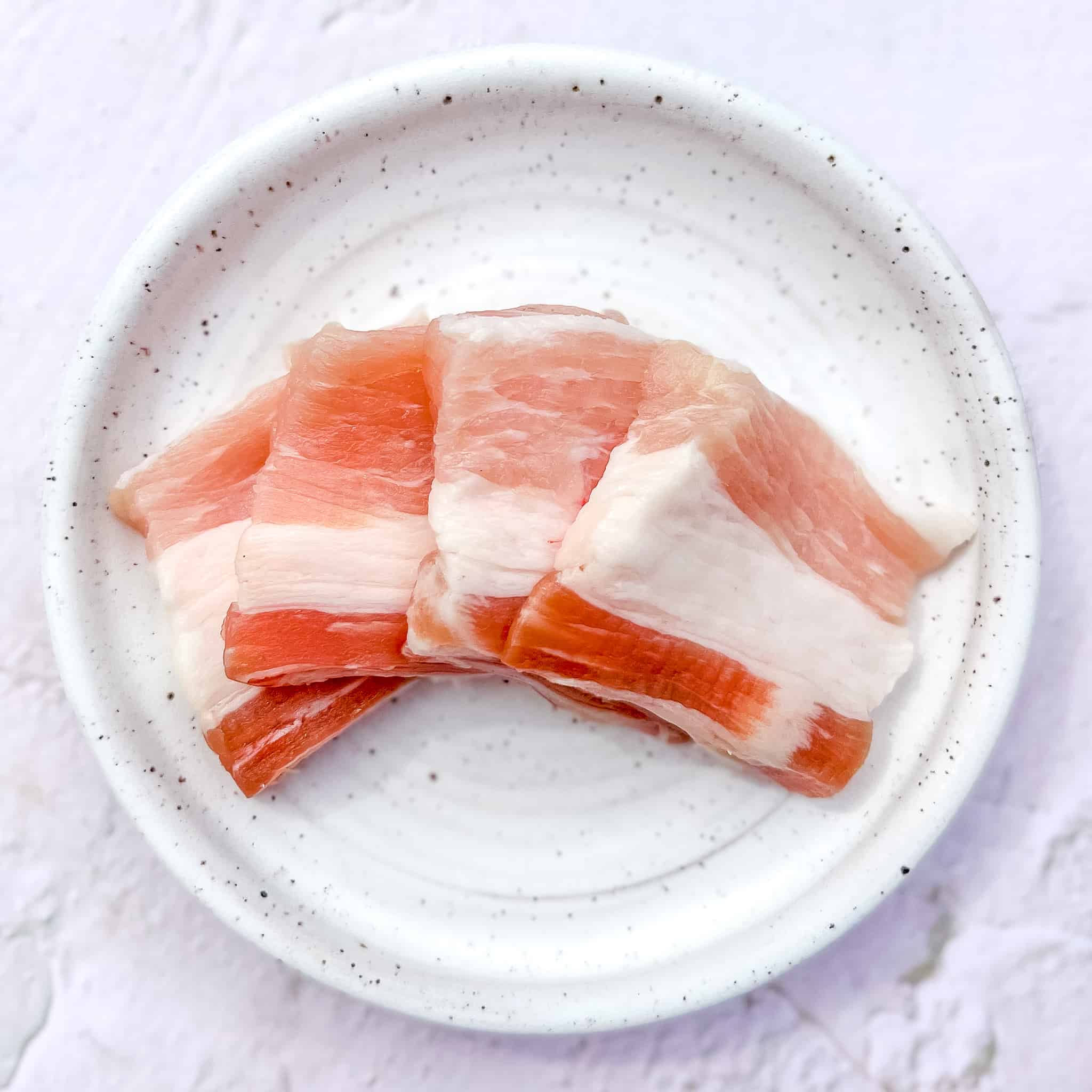 Slices of pork belly on a white plate.
