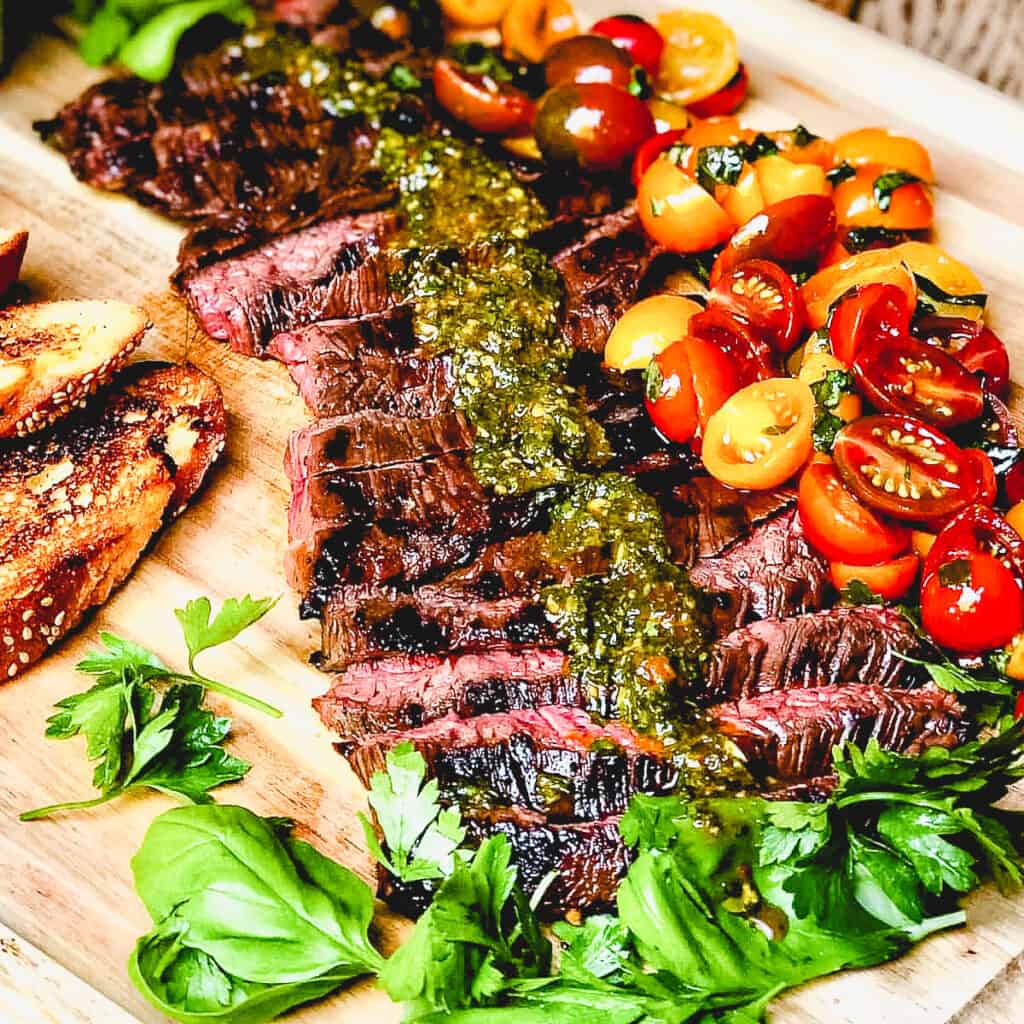 sliced steak with tomato salad on wooden cutting board.