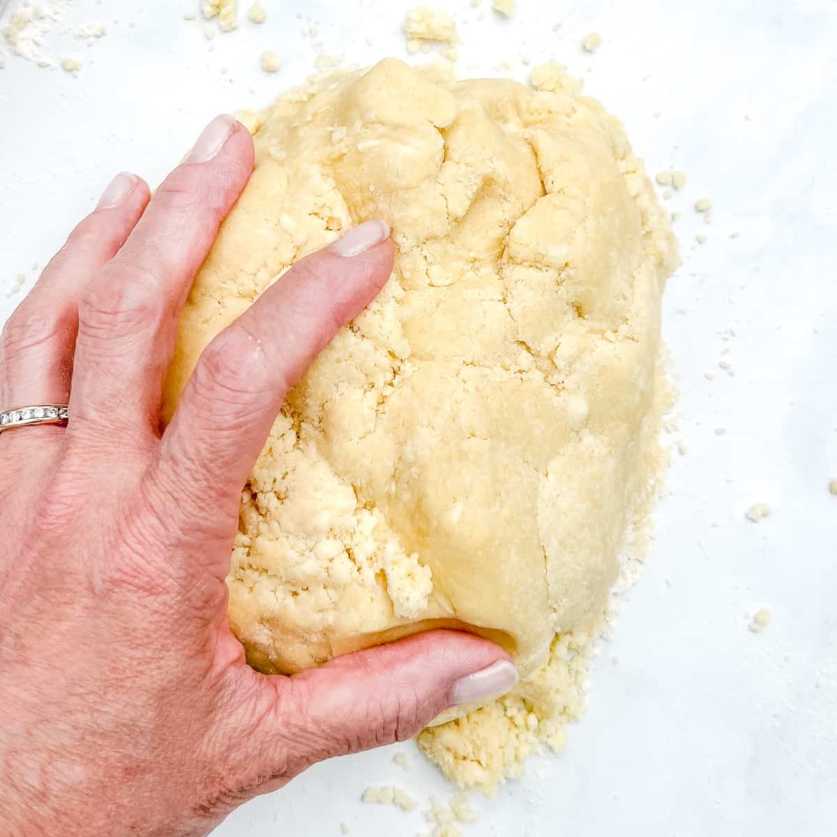 gathering crumbly pie dough together with hands.