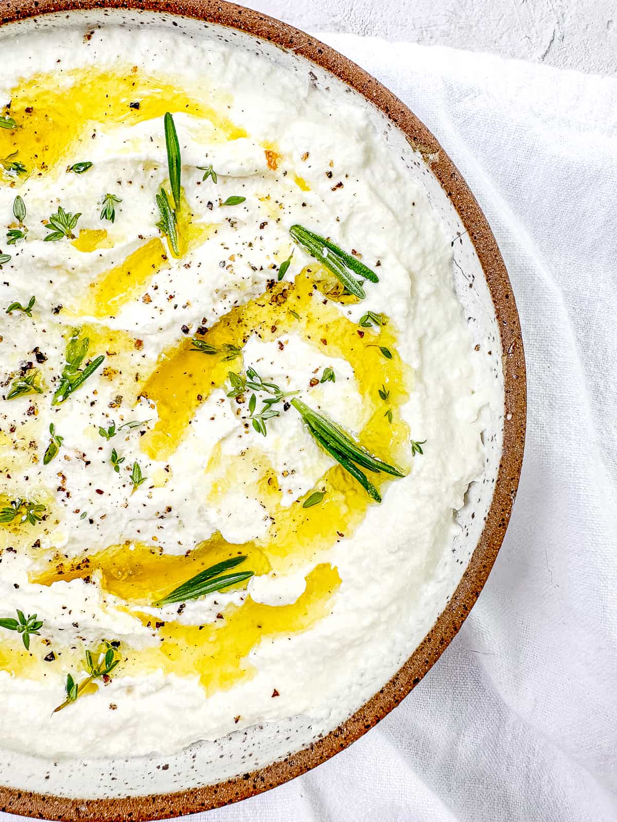 A bowl of 30 minute homemade ricotta with olive oil and herbs.