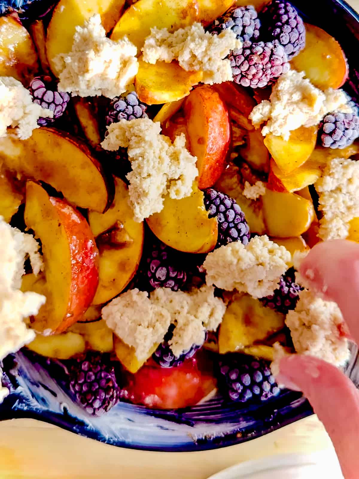 Breaking up biscuit dough over blackberry peach cobbler filling.