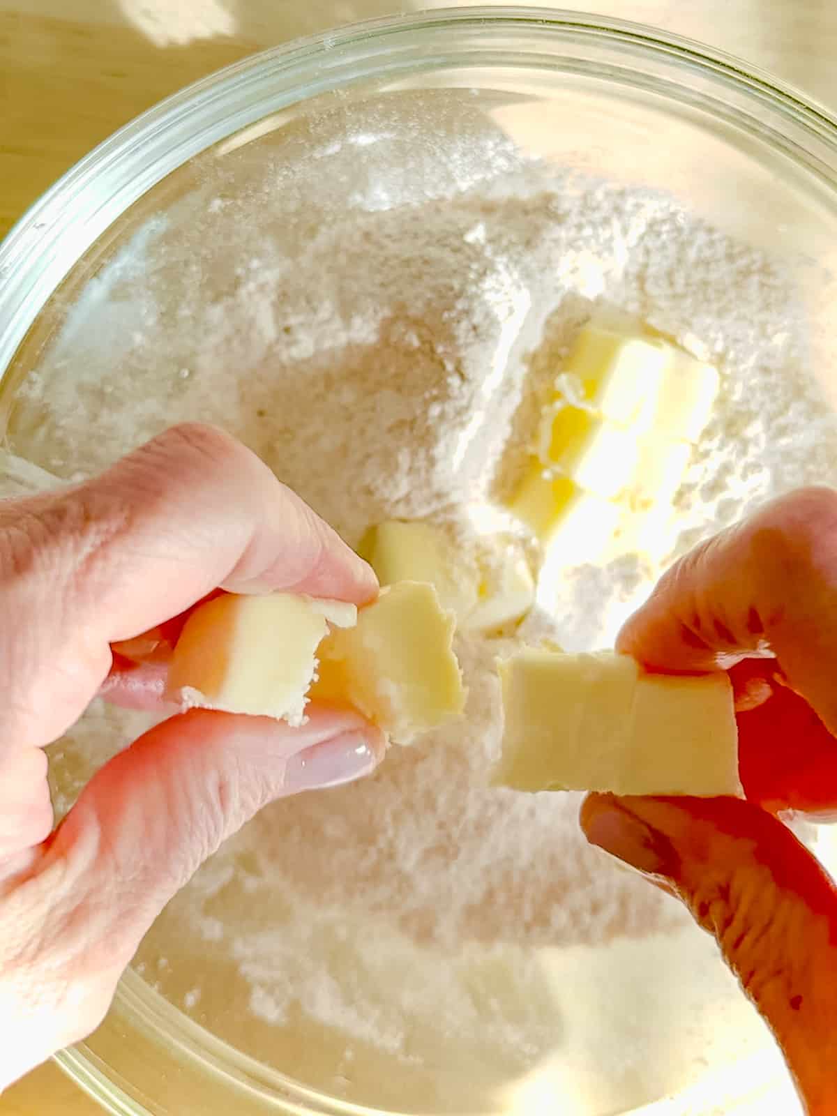 Breaking up butter cubes into flour and brown sugar in a bowl.