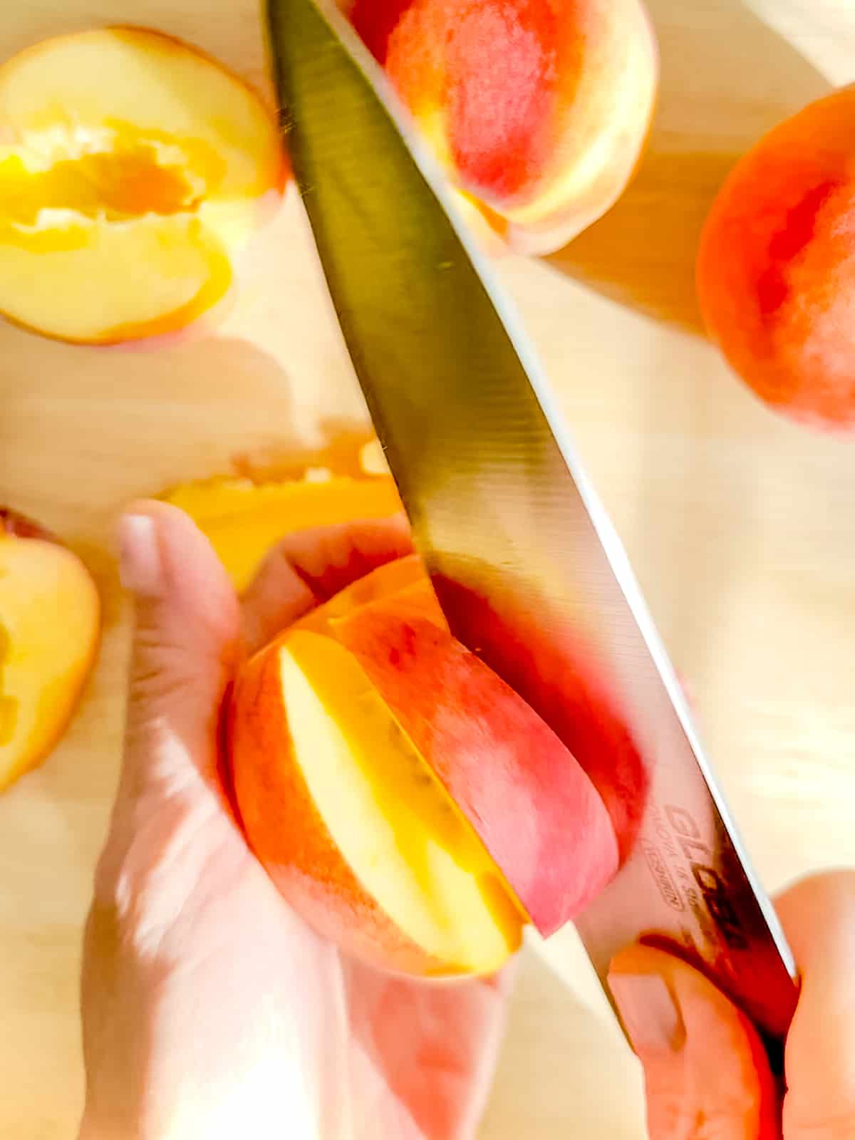 Using a chef's knife to slice a piece of peach off the pit.