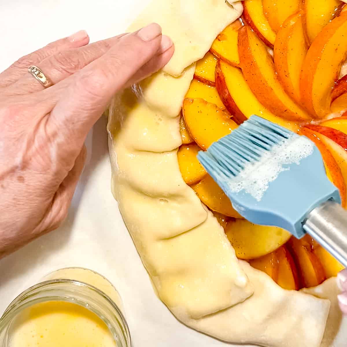 Brushing egg wash on the edge of a peach frangipane galette before baking.