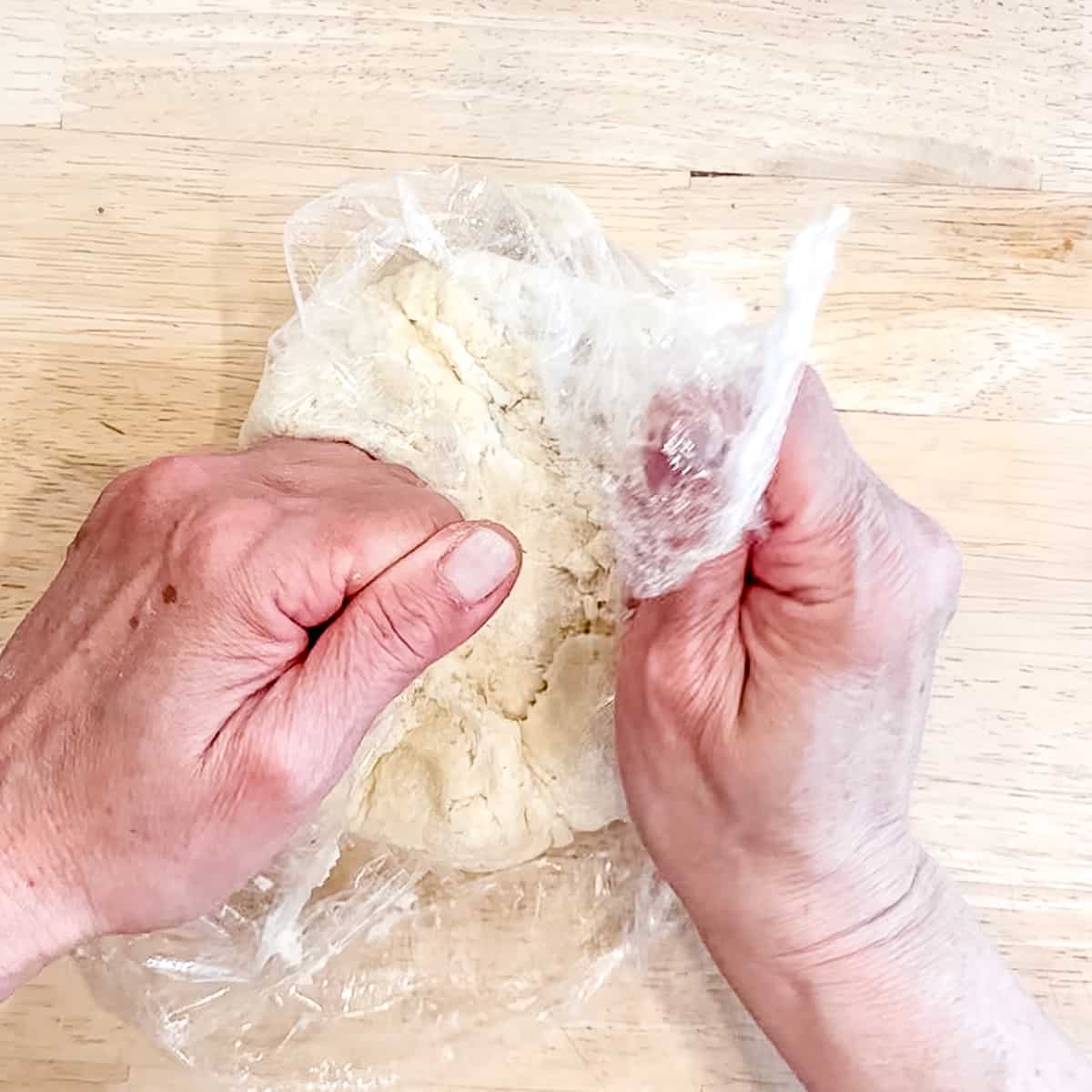 Using plastic wrap to gather pie crust together in a disc.