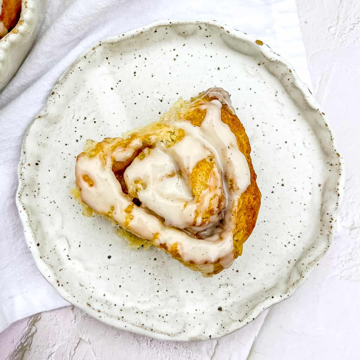 glazed biscuit cinnamon roll on a speckled white plate.