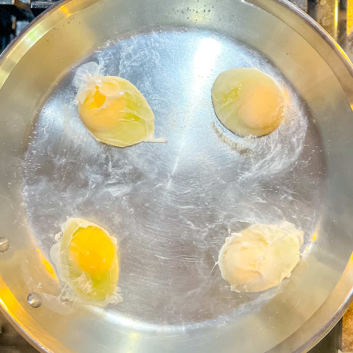 four poaching eggs in a pan.