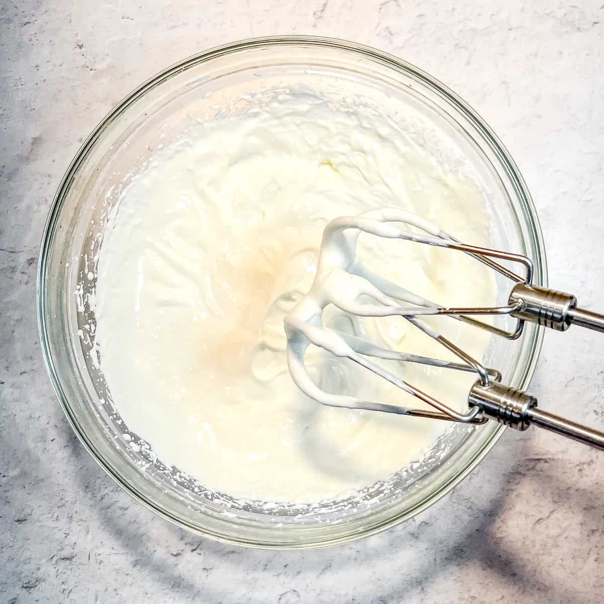 greek yogurt cream in a bowl with hand mixer.
