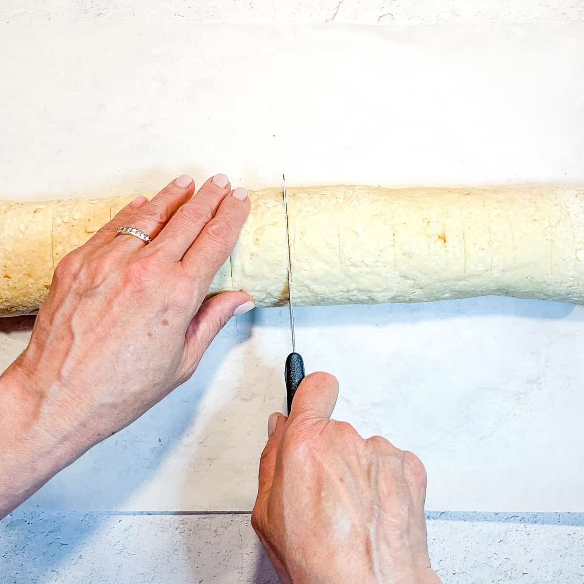 using a serrated knife to cut cinnamon roll log into individual rolls.