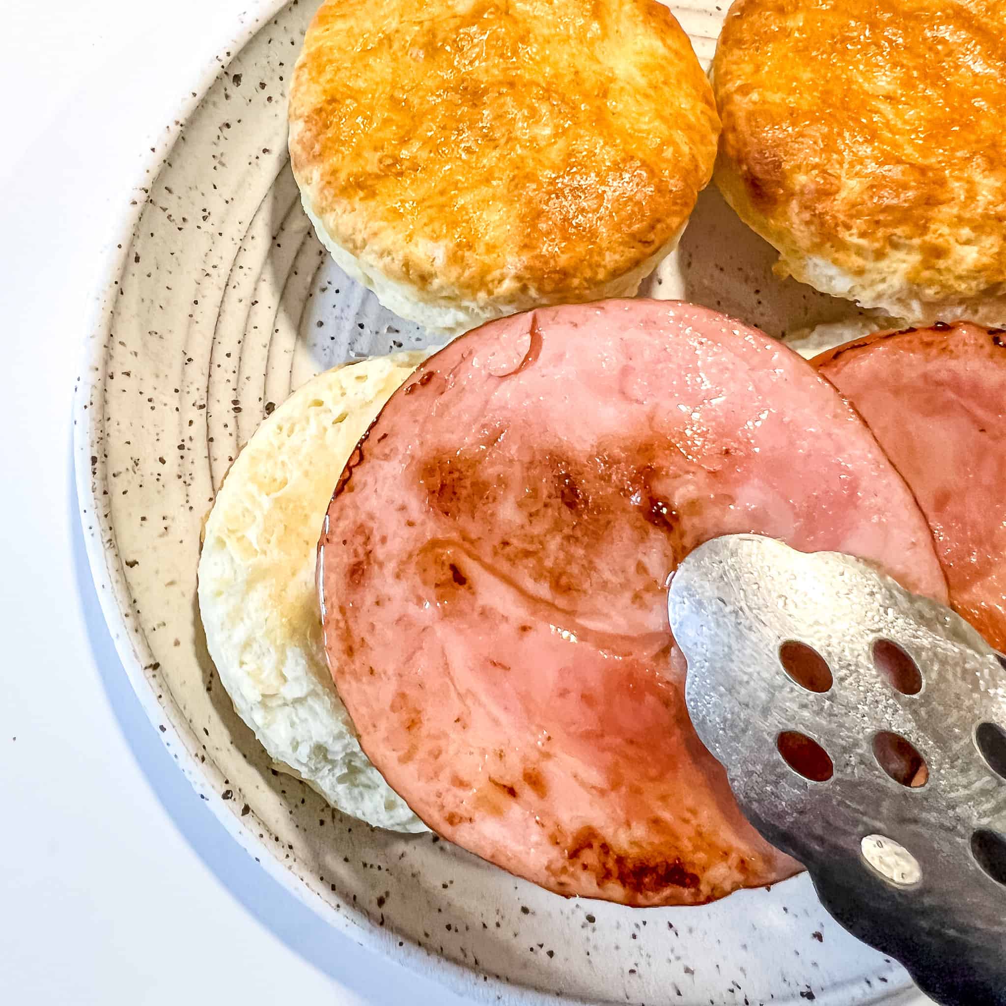 placing canadian bacon on a biscuit.