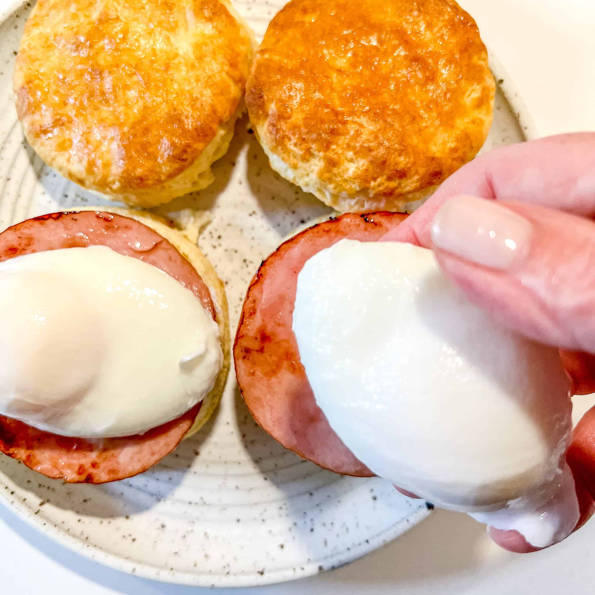 placing a poached egg on top of a biscuit with canadian bacon.