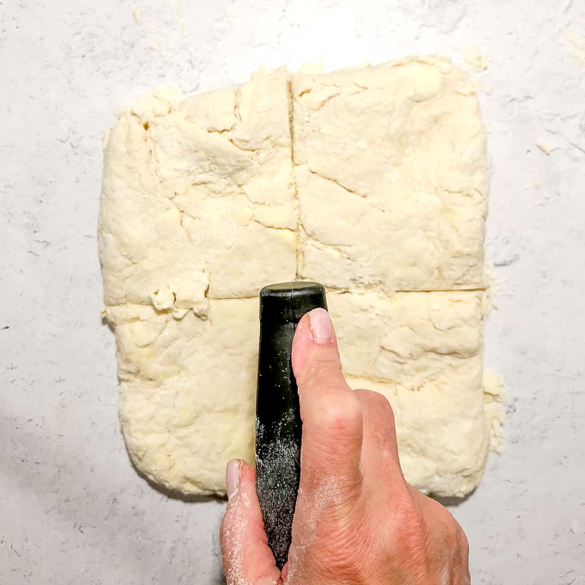 cutting biscuit dough into quarters with a bench scraper.