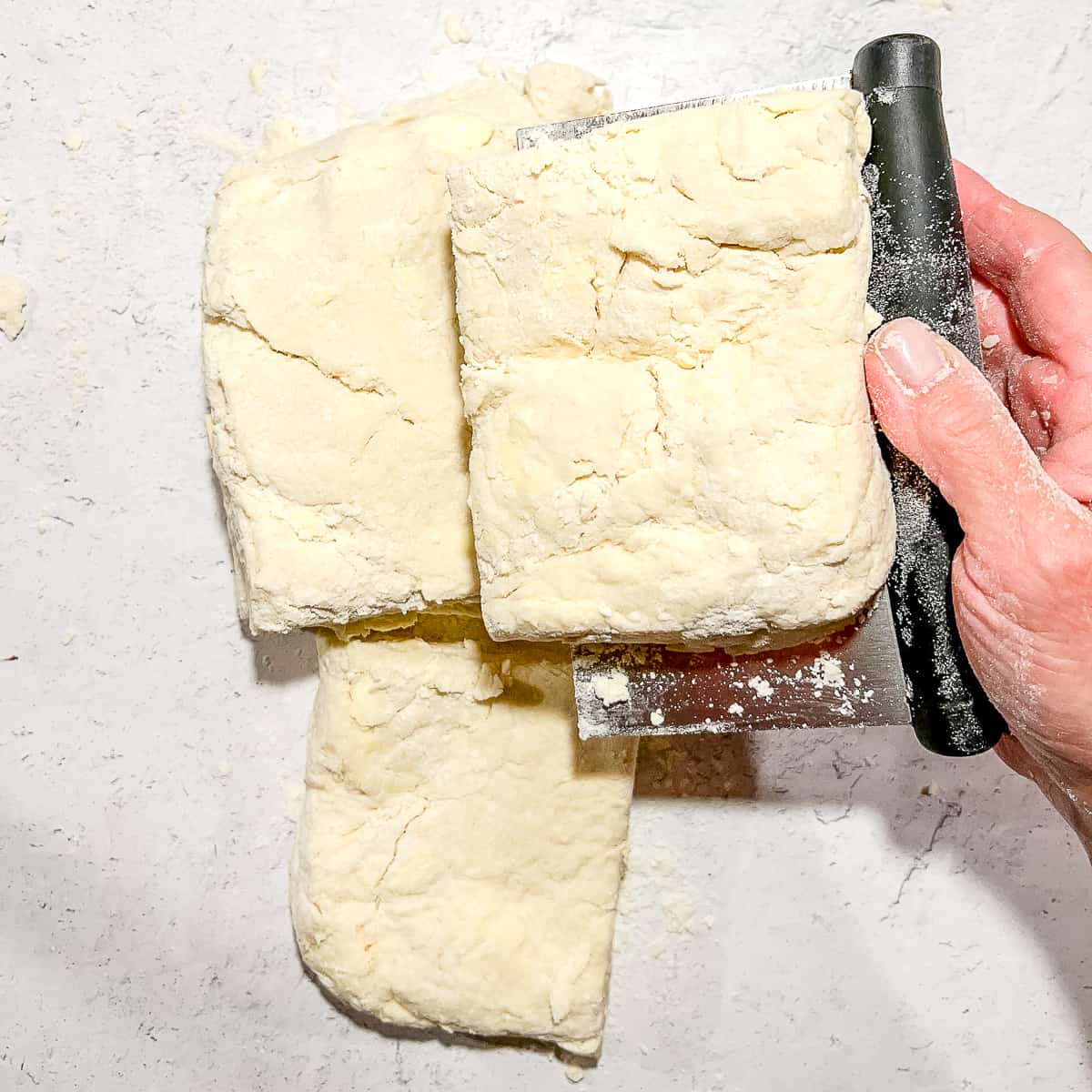 stacking quarters of biscuit dough using a bench scraper.