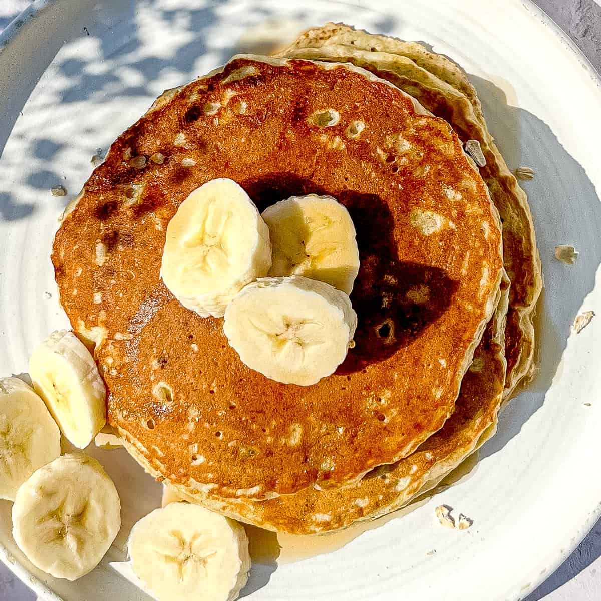 close up of banana oat pancakes with sliced bananas on a white plate.