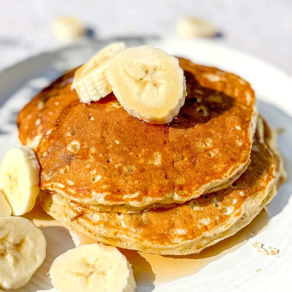 a tack of banana oat pancakes with sliced bananas and maple syrup.
