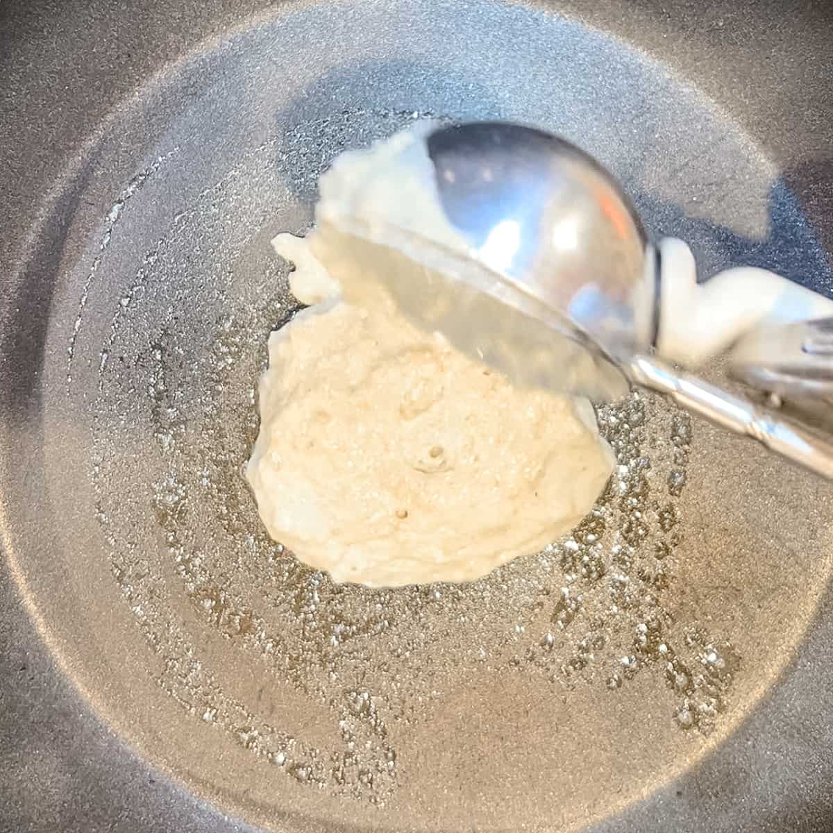using an ice cream scoop to portion pancake batter on to a skillet.