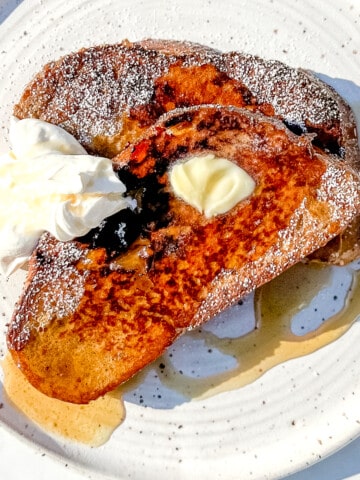 frecnh toast with yogurt whipped cream and maple syrup on a white plate.