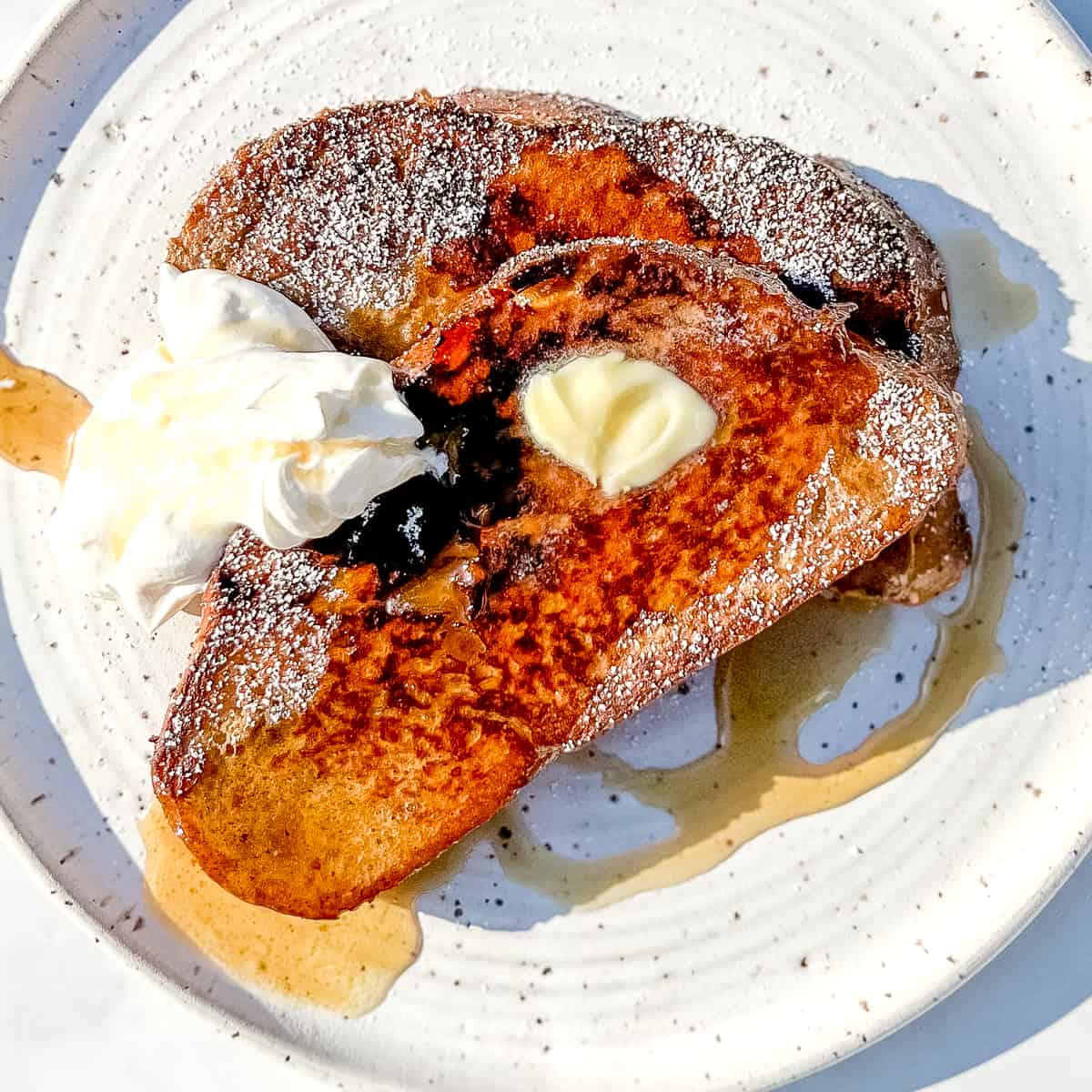 frecnh toast with yogurt whipped cream and maple syrup on a white plate.