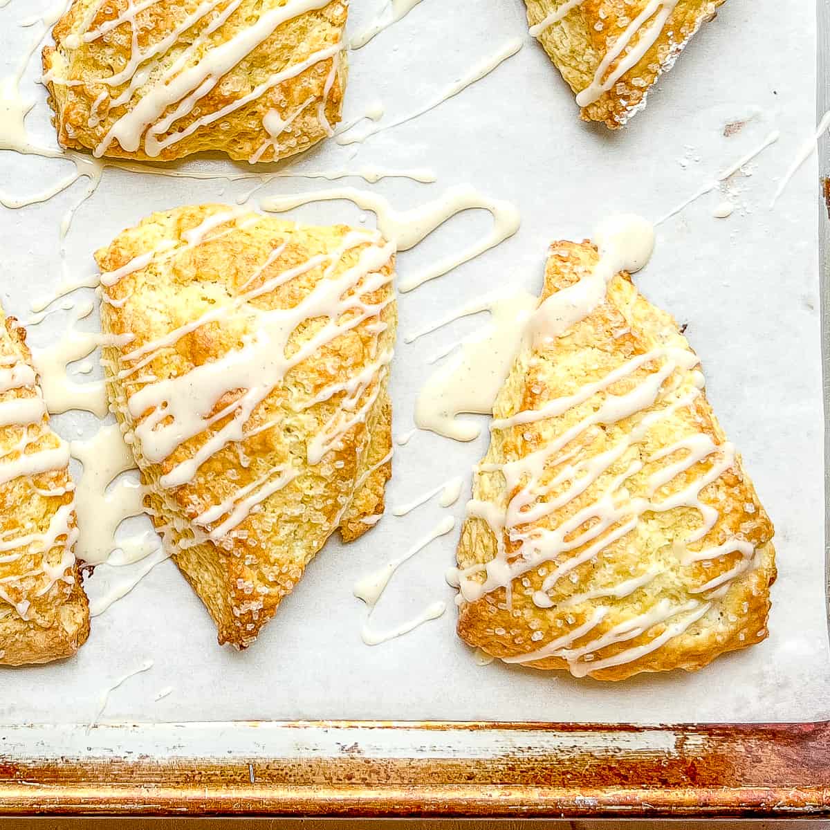 Orange scones with orange glaze on a baking sheet.