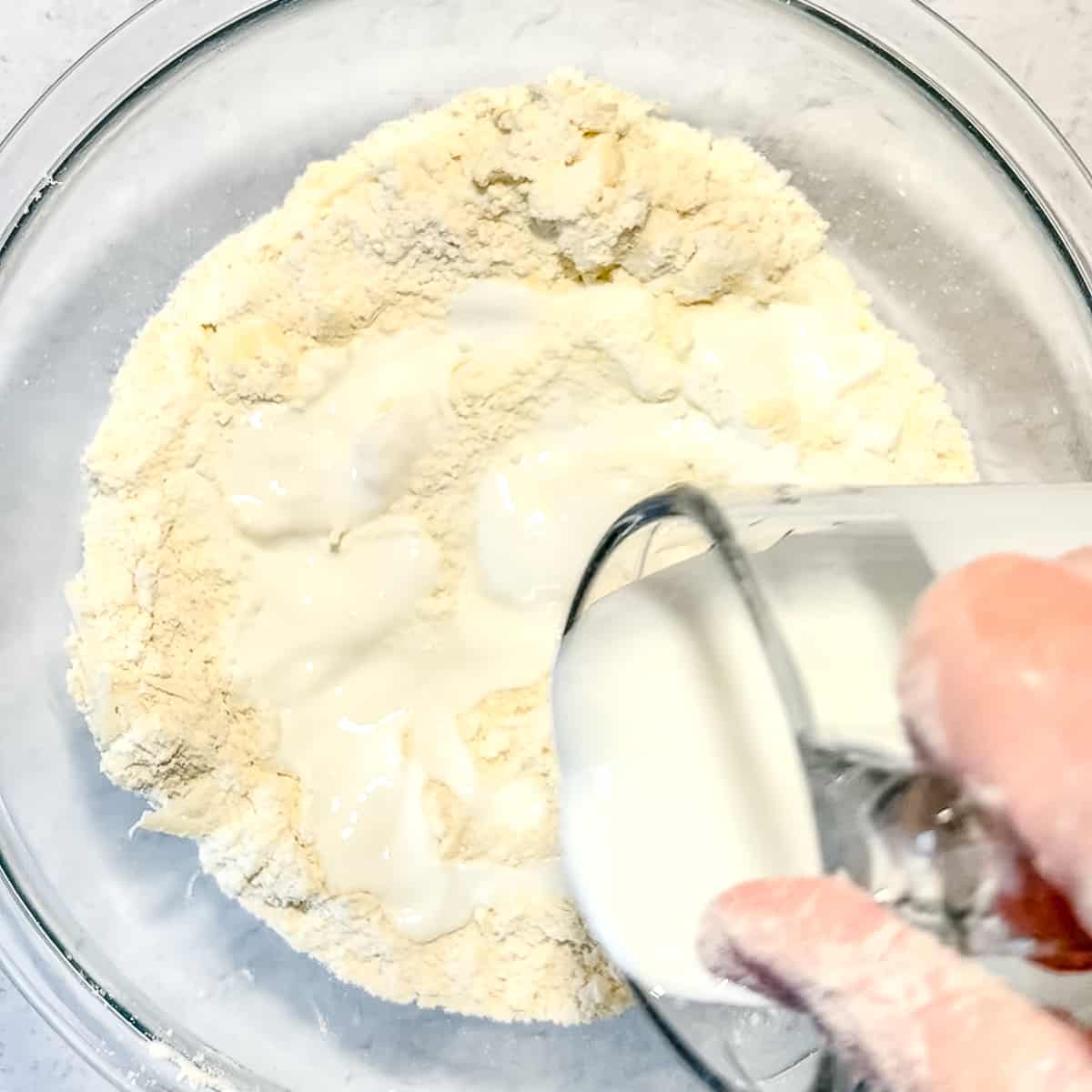 pouring buttermilk over biscuit dry ingredients.