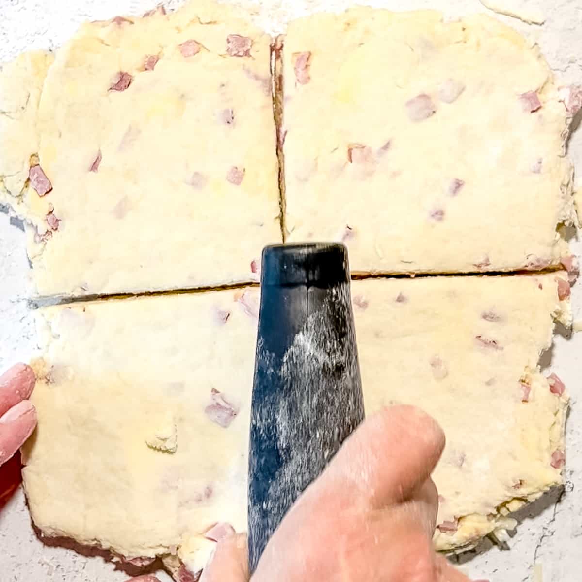cutting a large square of ham and swiss biscuit dough into 4 equal squares.