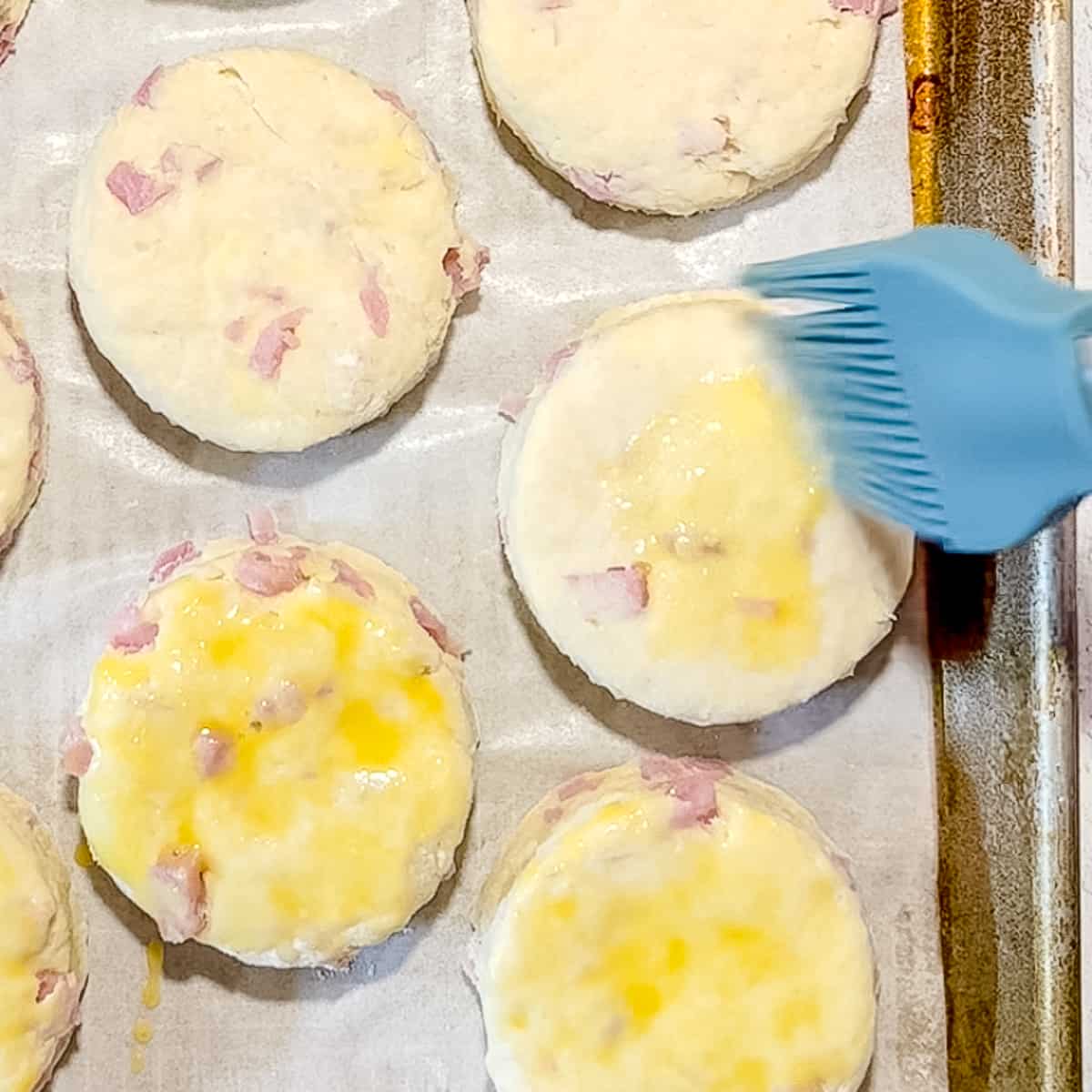 brushing egg wash on ham and swiss biscuits before baking.