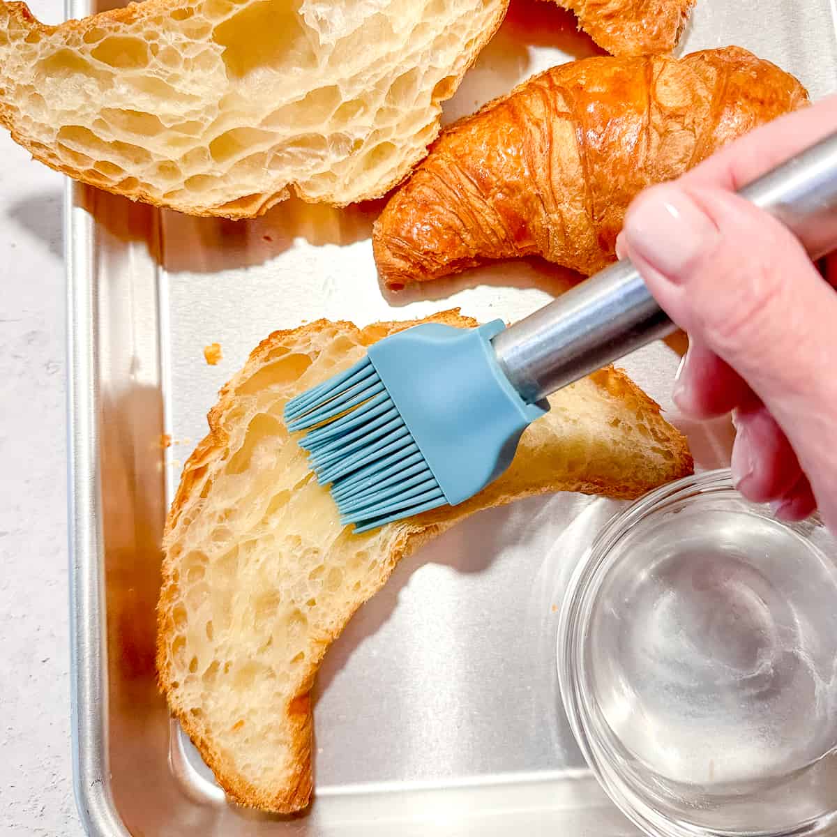 brushing almond syrup on the cut side of half a croissant.