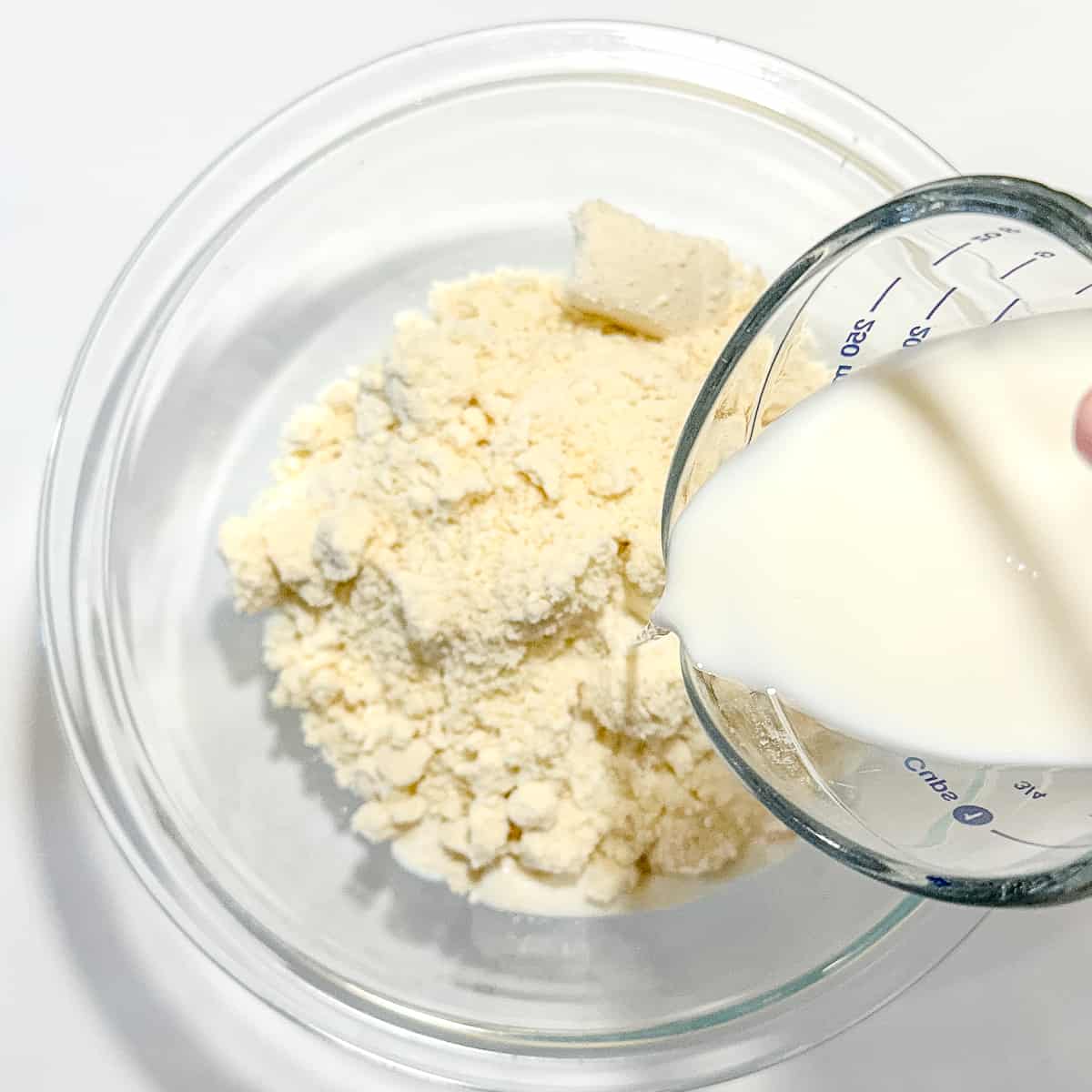 adding milk to a bowl containing buttermilk biscuit mix.