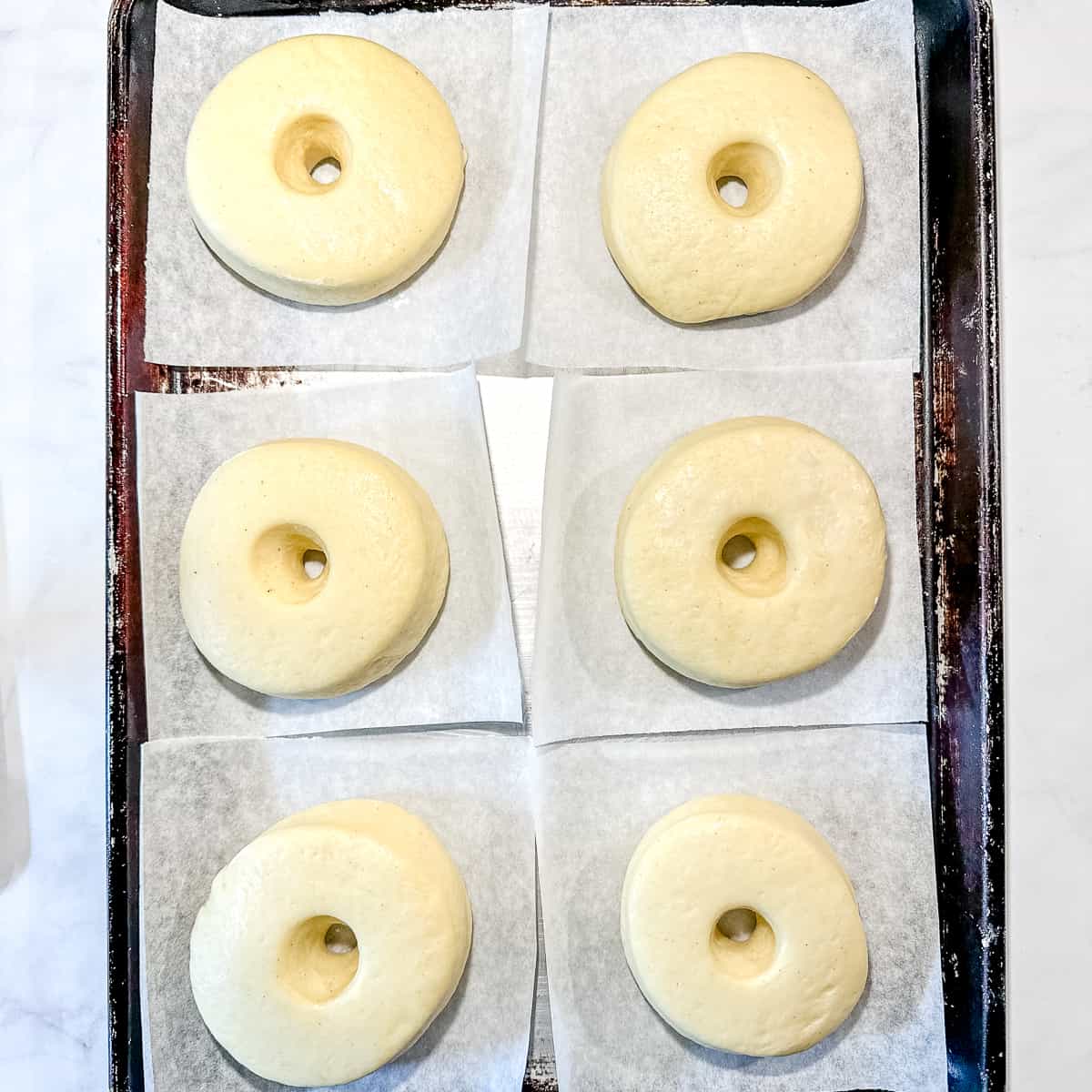 risen donuts on pieces of parchment paper/.