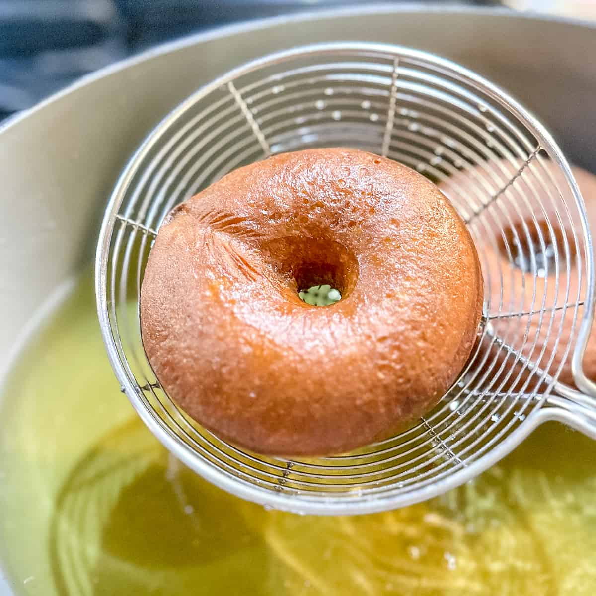 using a metal strainer to remove a fried donut from oil.