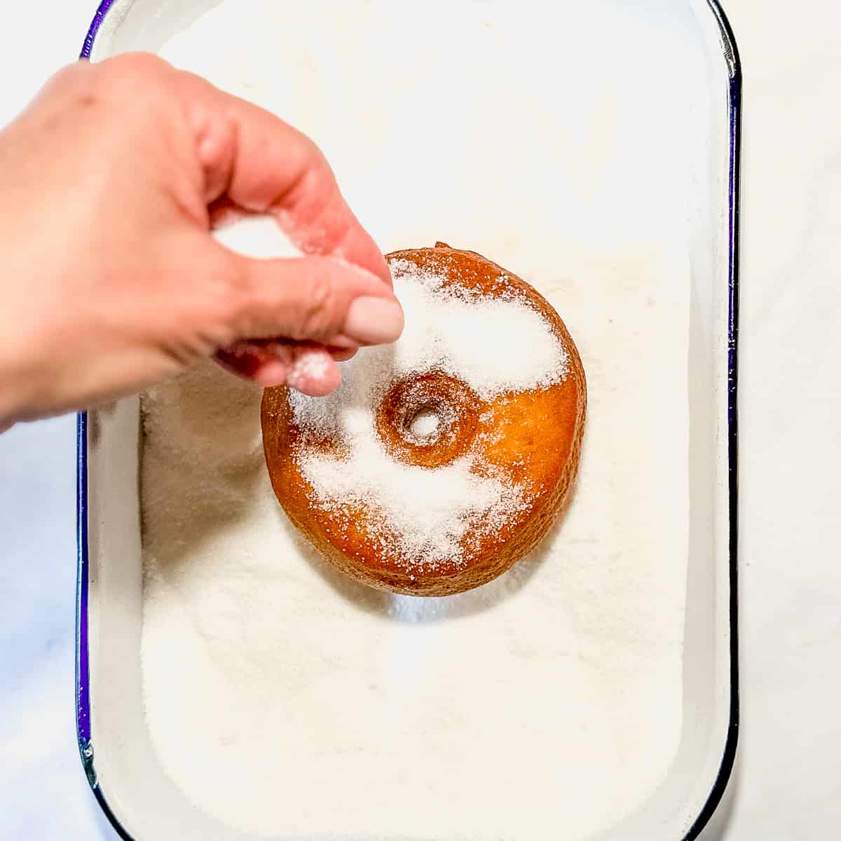 sprinkling sugar on a fried donut.