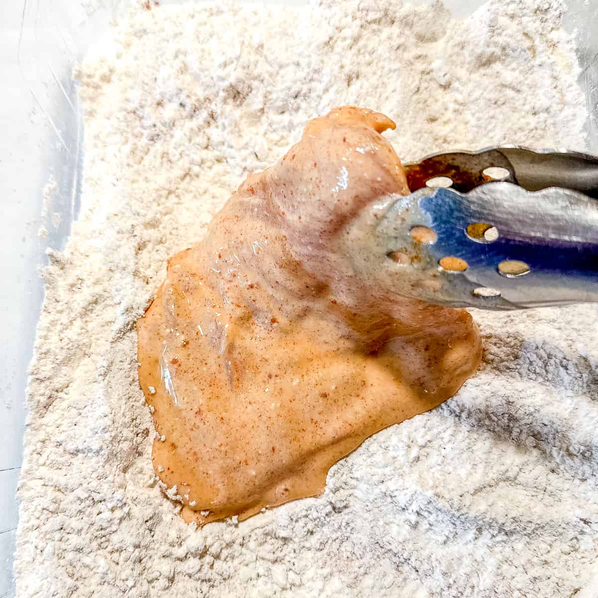 dredging a piece of chicken in flour and spices.