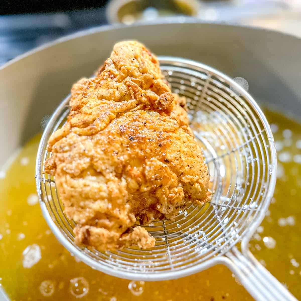 using a spider strainer to remove a piece of fried chicken from oil.