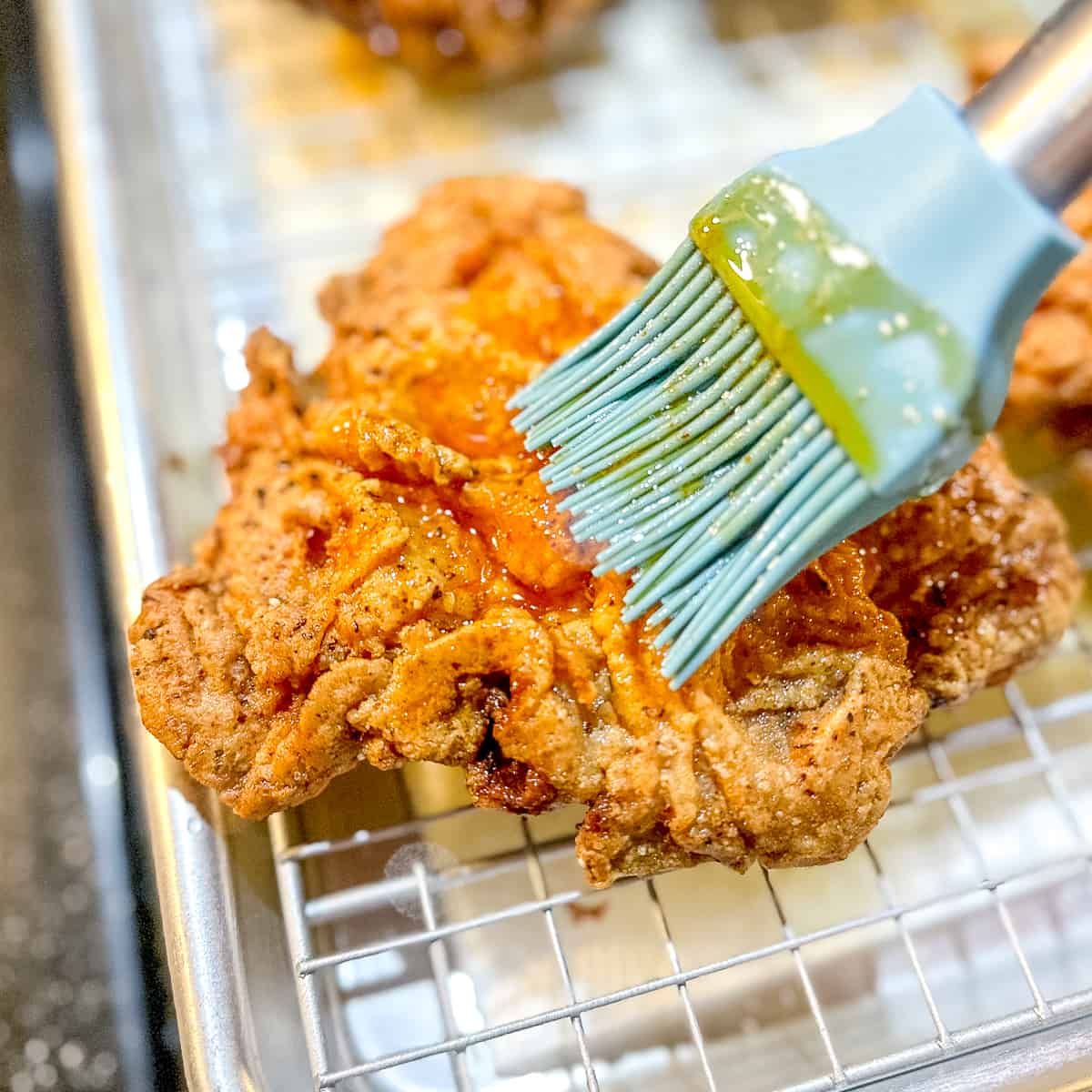 brushing spicy maple honey butter on a piece of fried chicken.