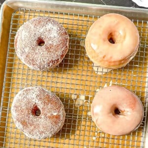 Glazed and sugar raised donuts on a wire rack.