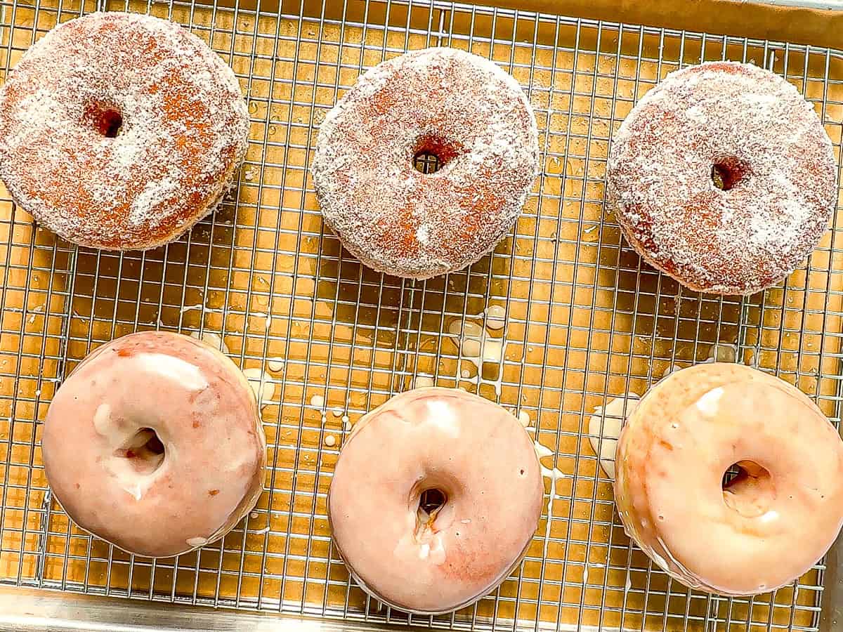 Glazed and sugar raised donuts on a wire rack.