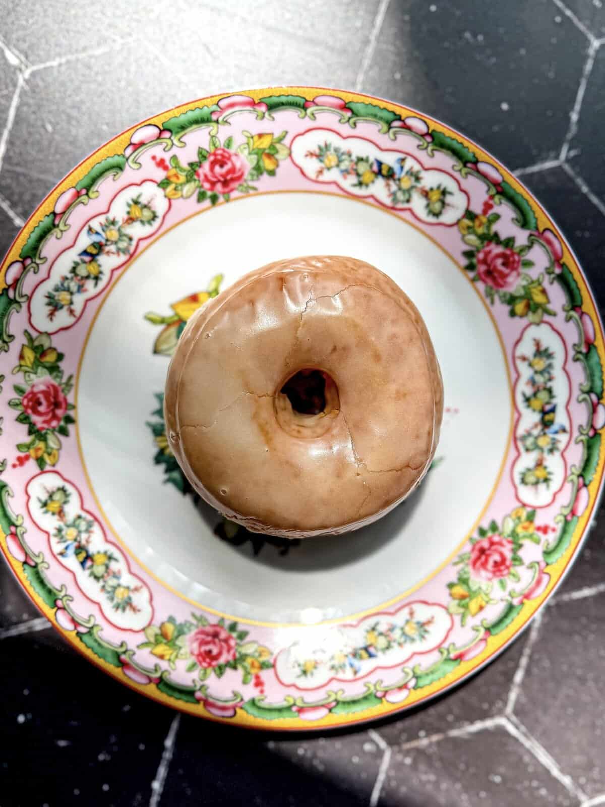 Glazed donut on a floral plate.
