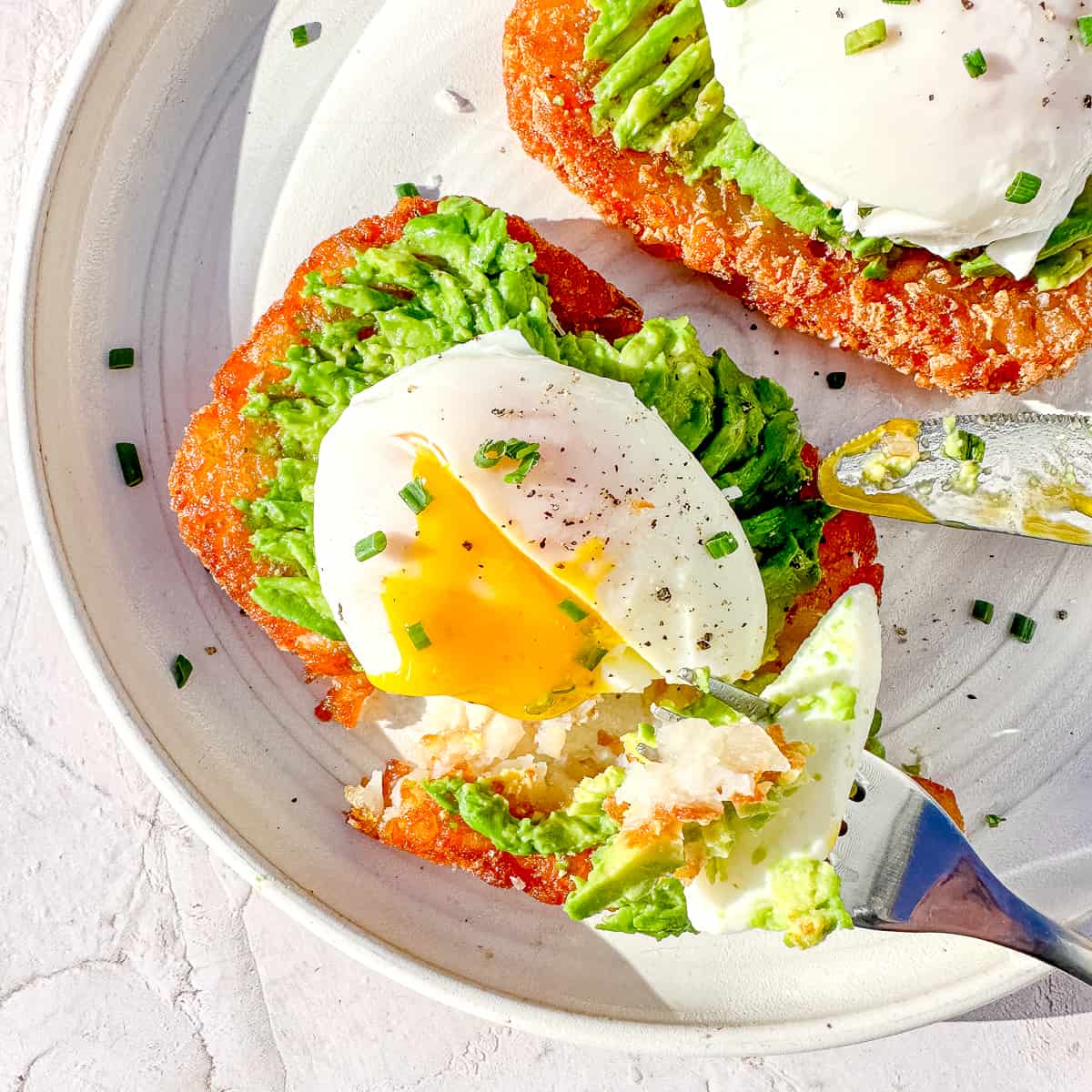 cutting into poached egg on top of hash brown patty with avocado.
