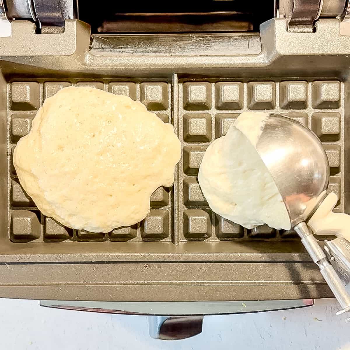 adding a scoop of waffle batter to waffle maker.