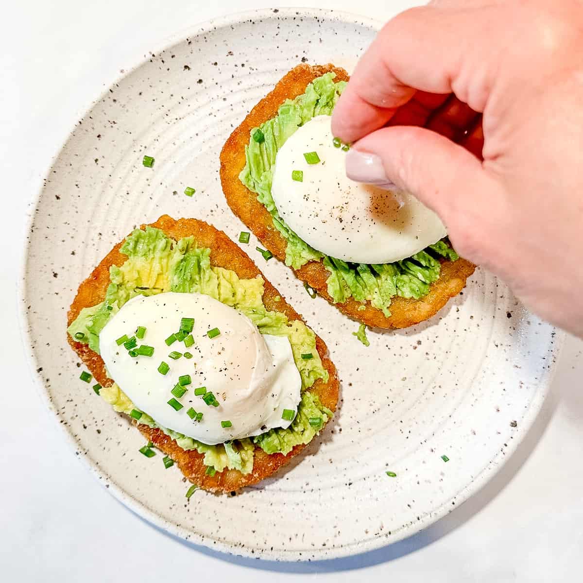 sprinkling chives on top of hash brown avocado toast.