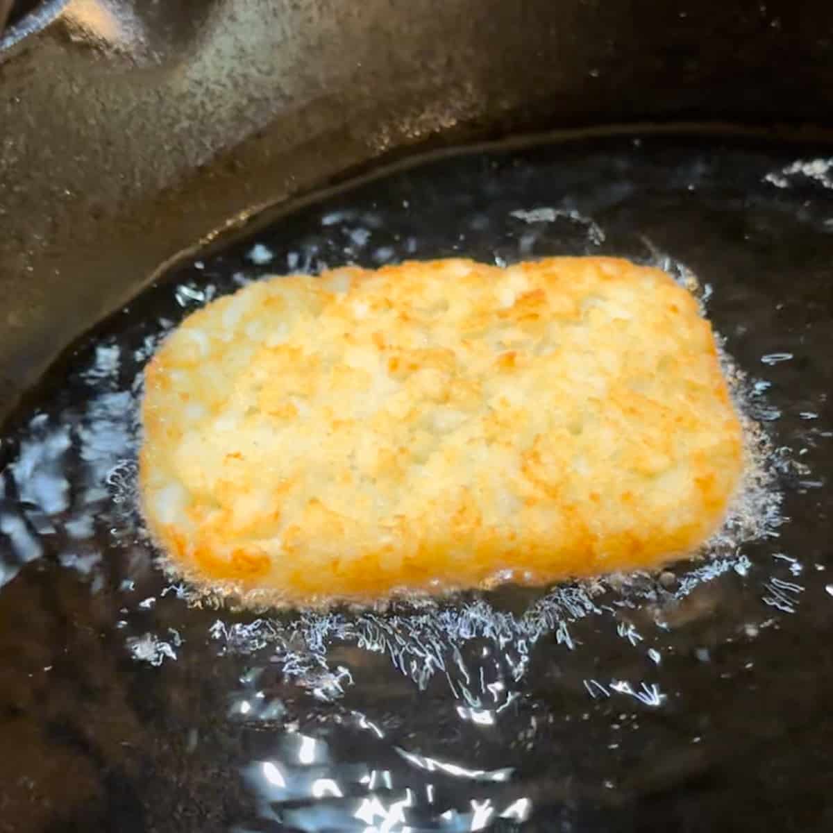 shallow frying a hash brown patty in a cast iron pan.