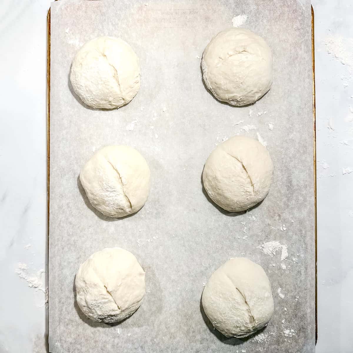 placing slashed dough balls on a piece of parchment paper placed on the back of a sheet pan.