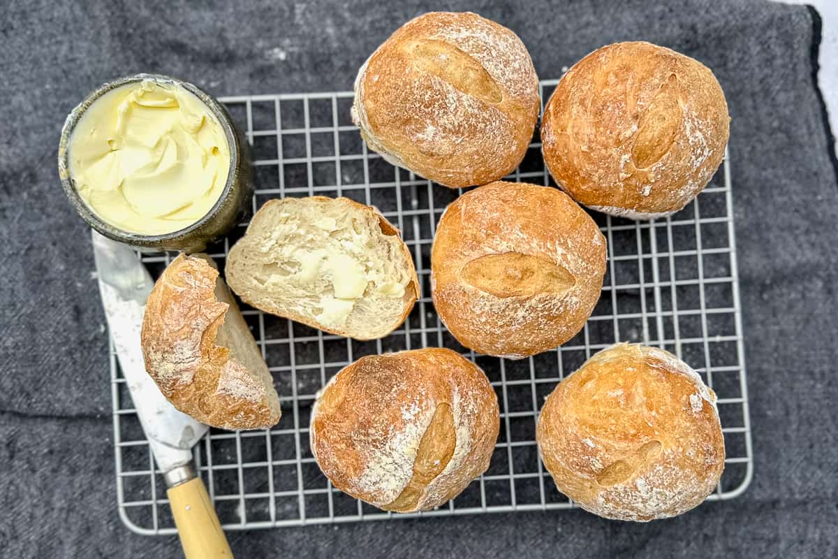 crusty rolls on a wire rack with one cut open and buttered.