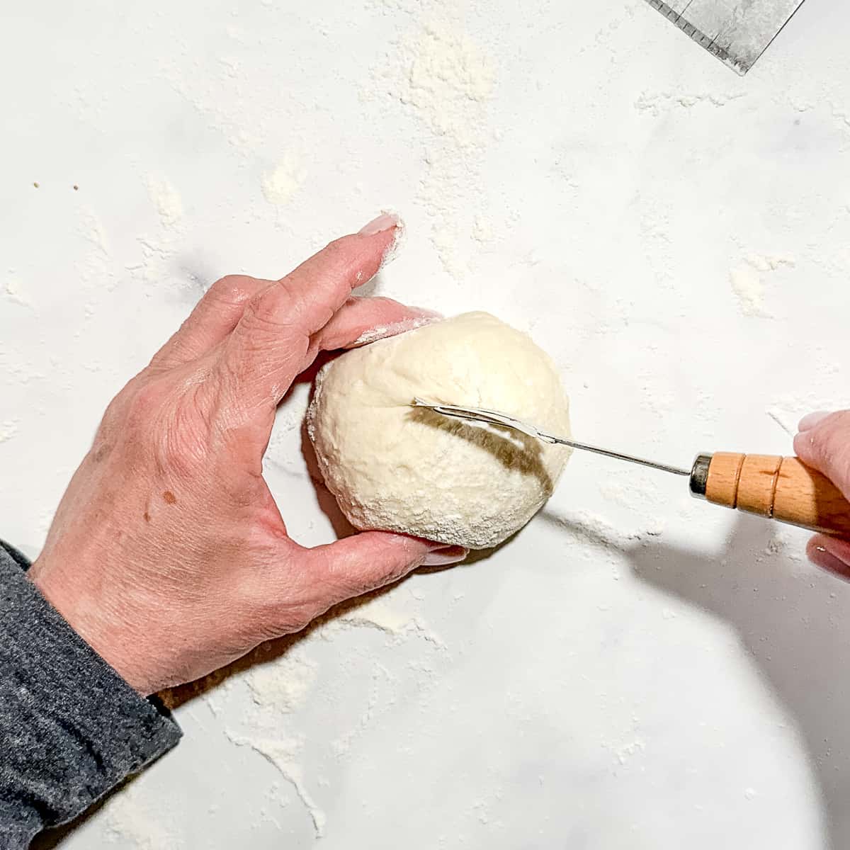 using a bread lame to slash a dough ball before baking.