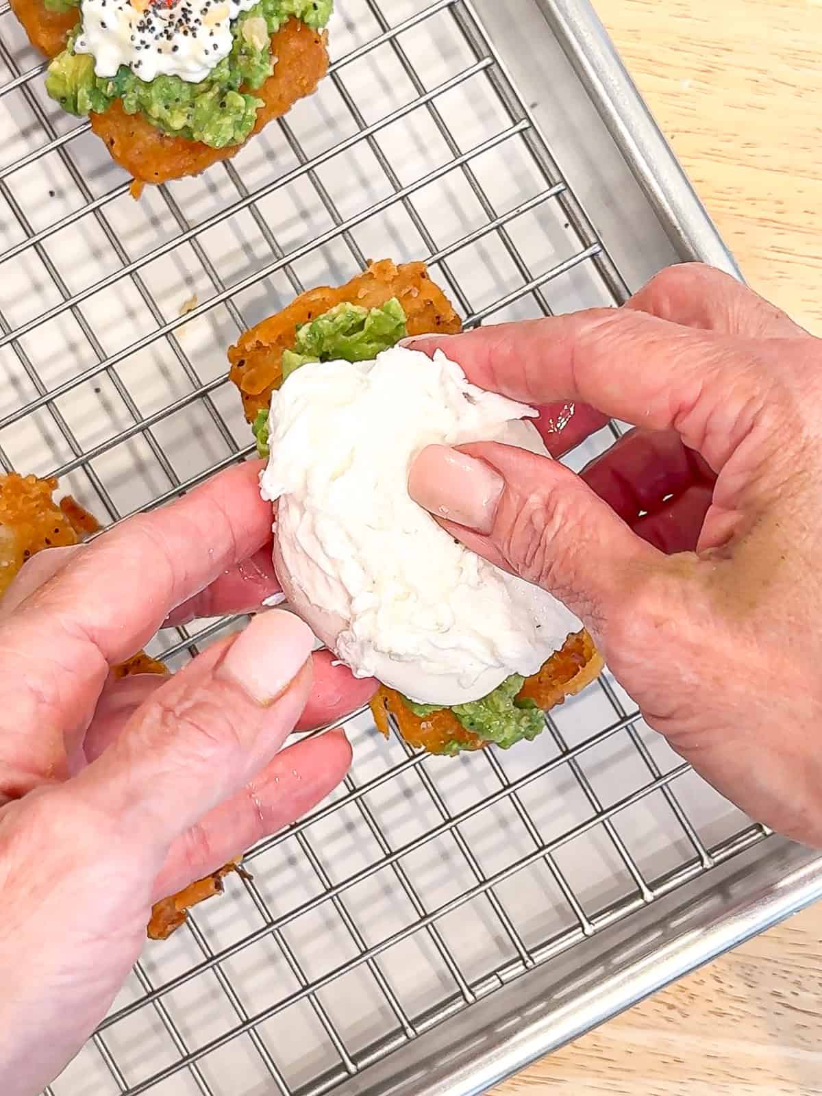Placing a poached egg on a hash brown with mashed avocado.
