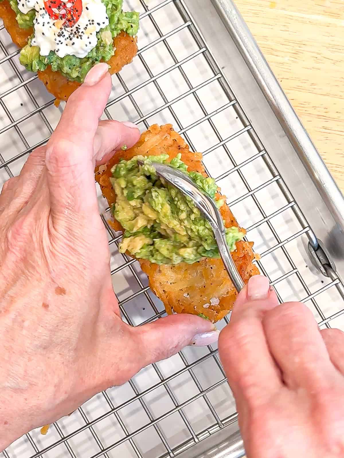 Placing mashed avocado on a hash brown.