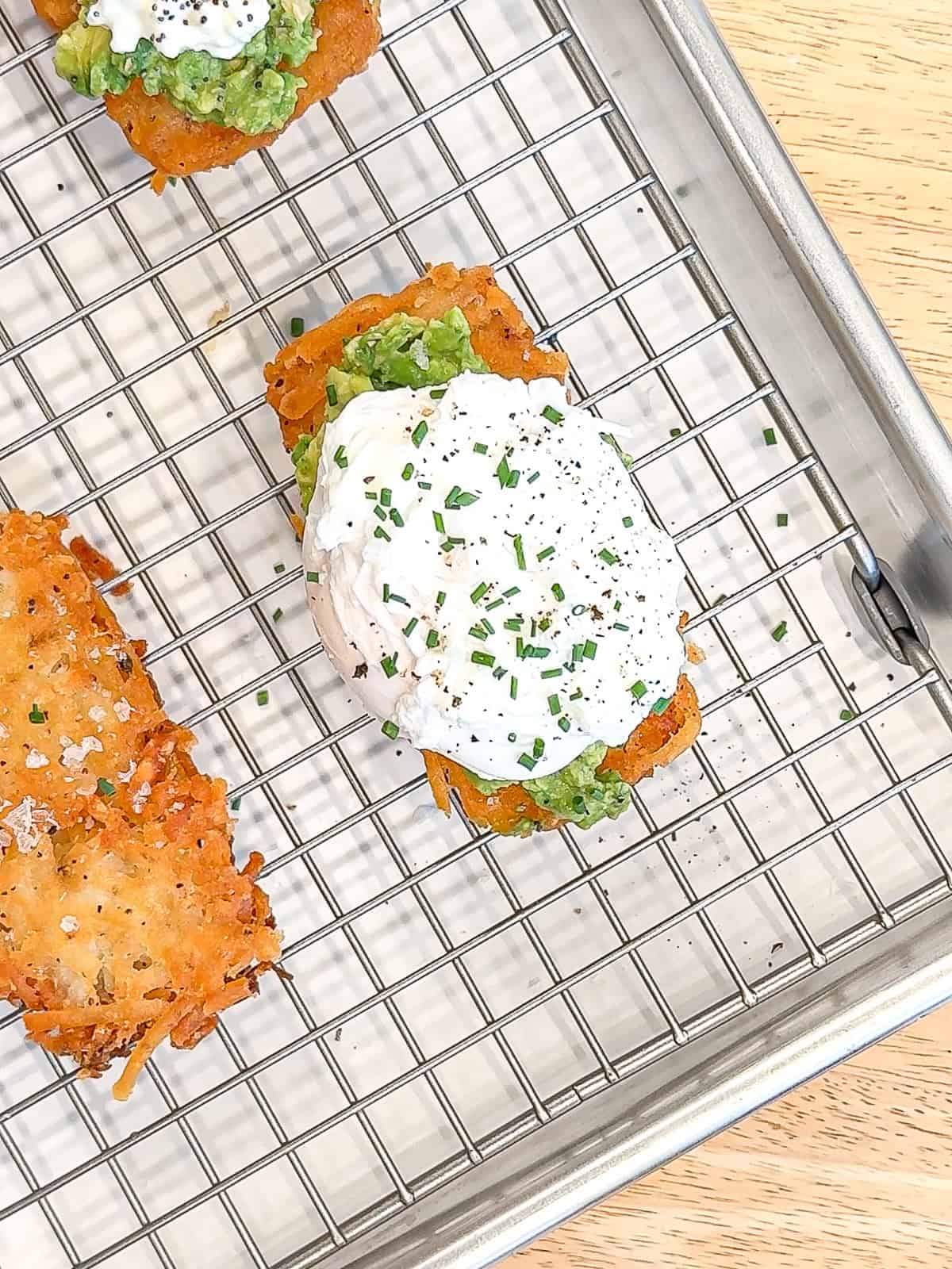 A poached egg with chives on a hash brown with mashed avocado.
