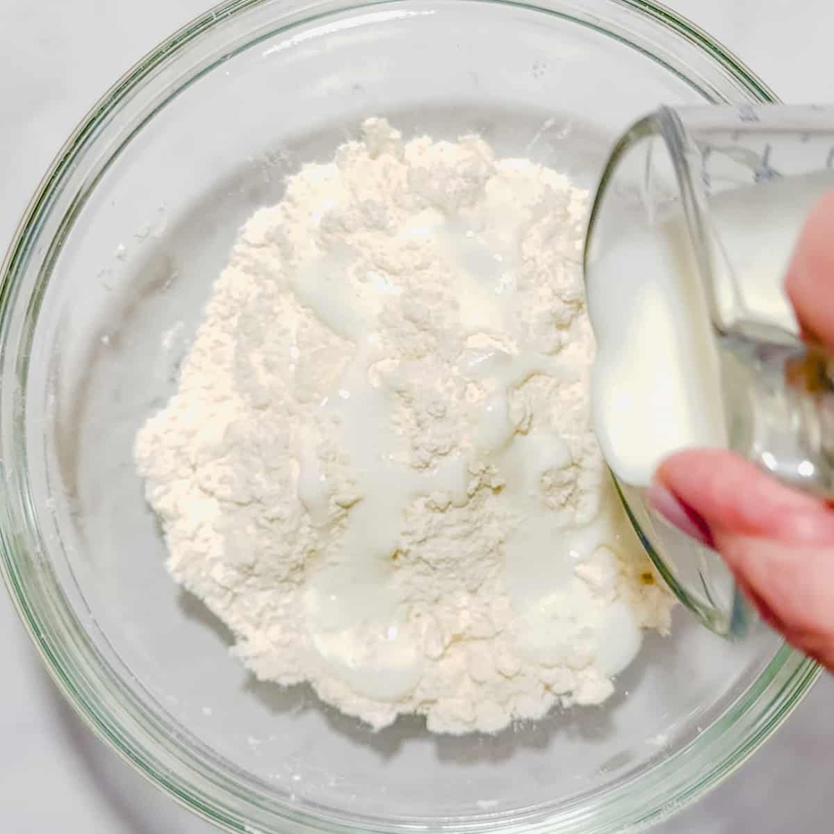 pouring buttermilk into dry biscuit ingredients.