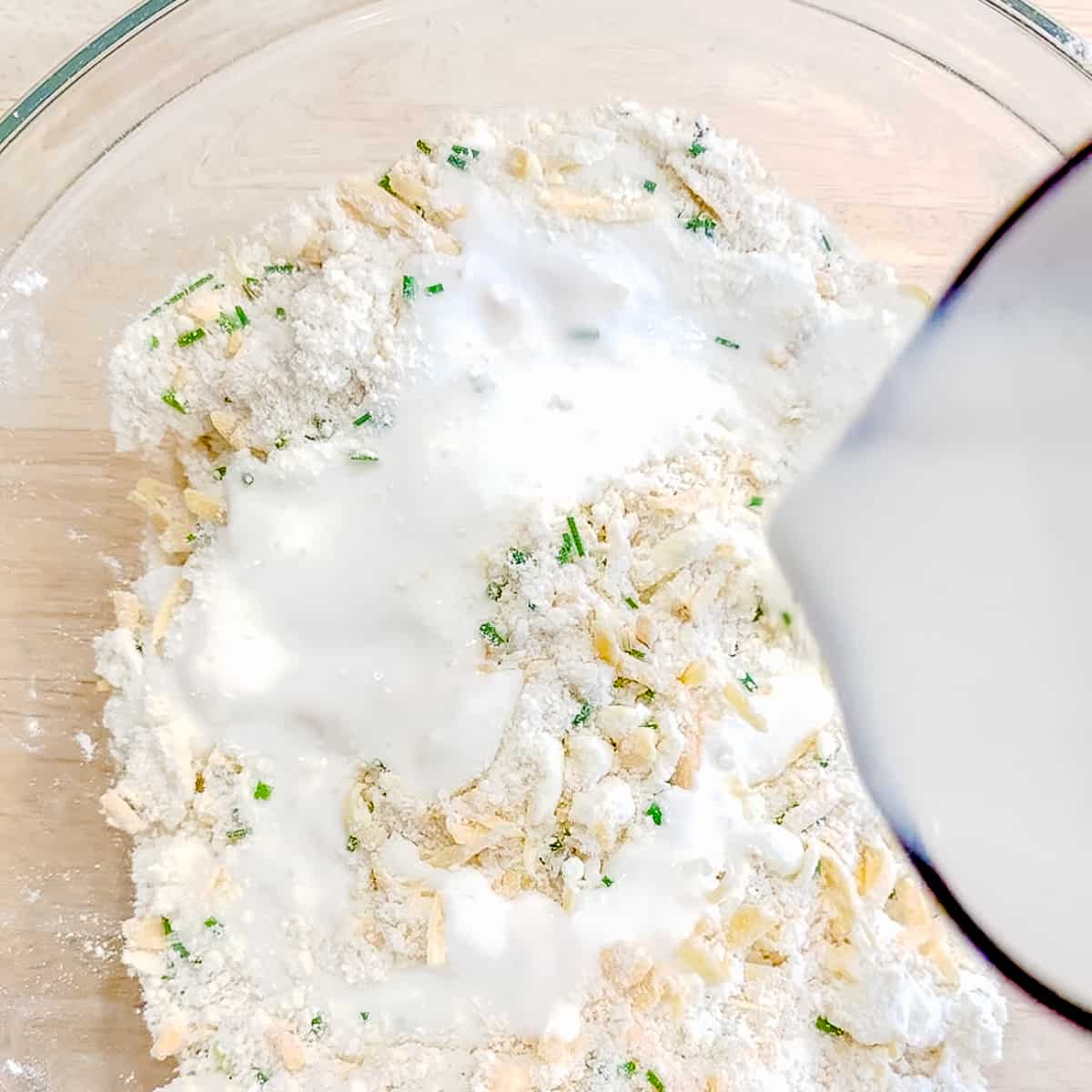 pouring buttermilk into chaddar chive biscuit ingredients.
